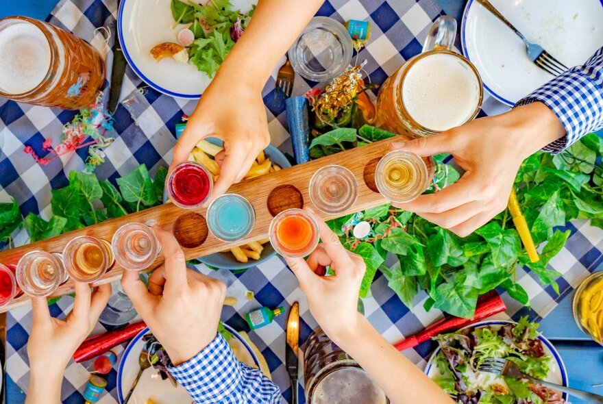 Looking down at a table from above where a long beer flight is being served with hands grabbing glasses. 