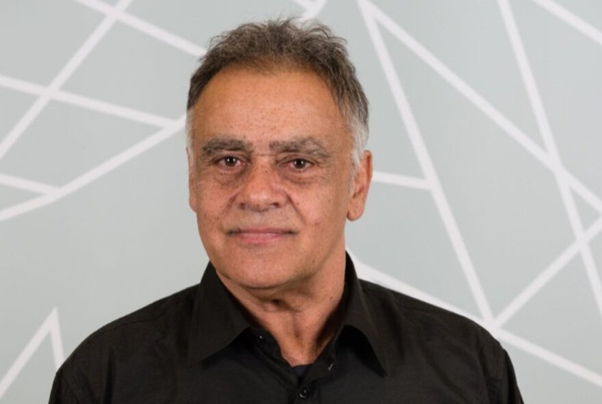 A portrait of Dr Paul Collis, smiling slightly against a grey and white patterned background. 