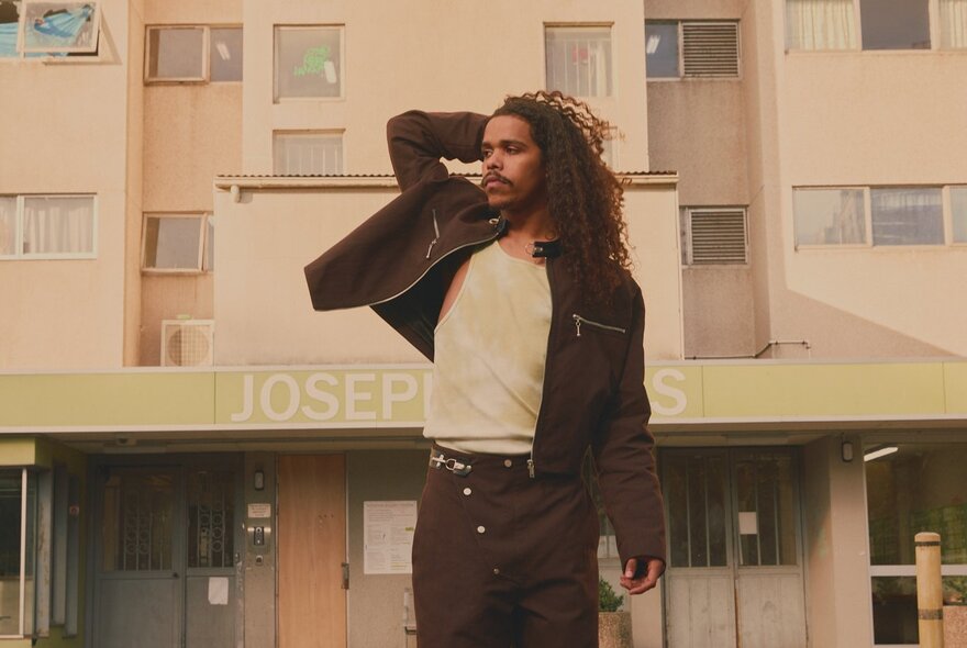 Musician Dean Brady with arm raised behind his head, wearing casual dark jacket and trousers.
