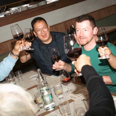 A slanted view of people at a table raising glasses of red wine in a toast. 