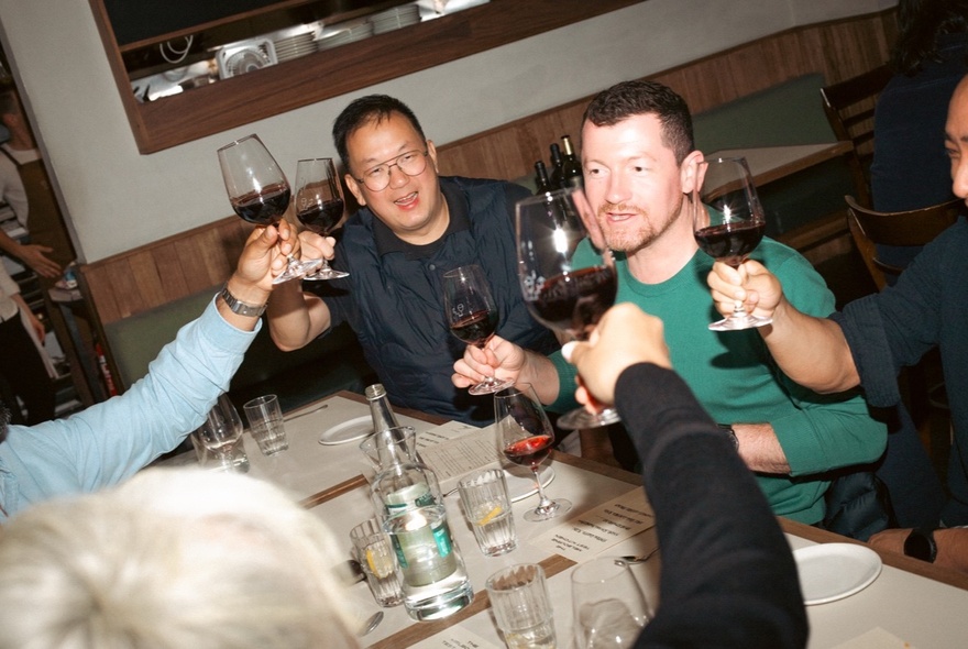 A slanted view of people at a table raising glasses of red wine in a toast. 