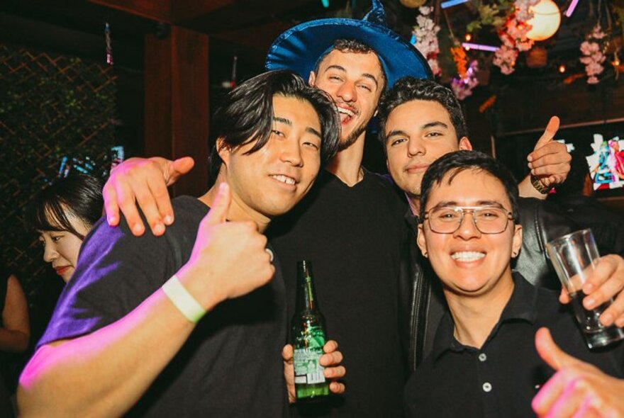 Multicultural young men posing with thumbs up, holding drinks.