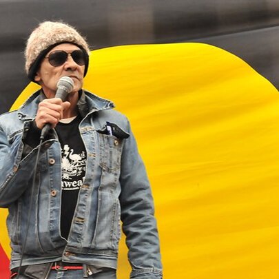 Australian Aboriginal political activist Robbie Thorpe, holding a microphone in front of the Aboriginal flag.