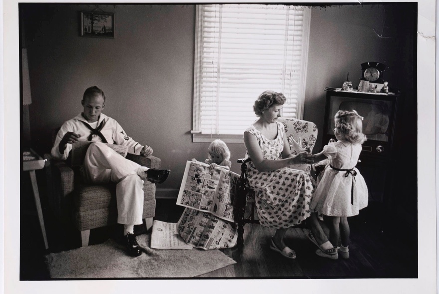Domestic interior portrait of a family in a lounge room, the father in Navy uniform, the mother playing with two children.