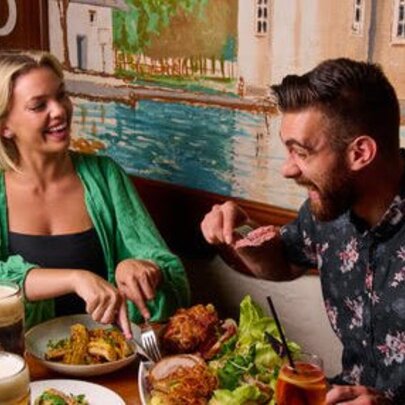 A couple eating at a restaurant with plates of food in front of them and a painted mural on the wall behind their table.