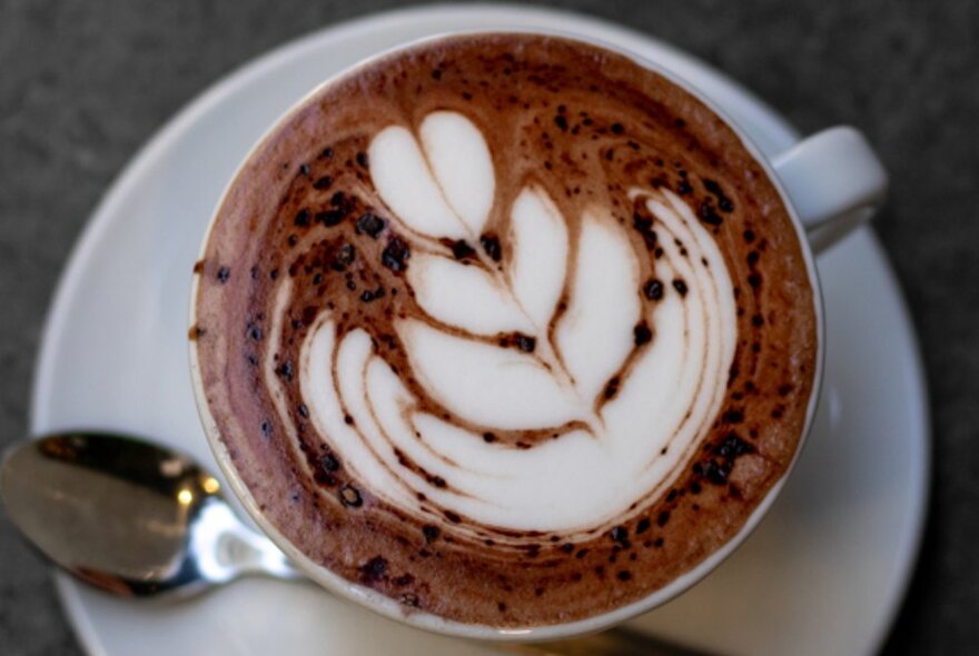 A frothy cappuccino in a cup with a feathered pattern in the milky chocolate foam.