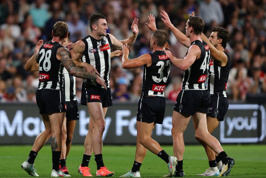 Five Collingwood football players high-fiving on the field. 