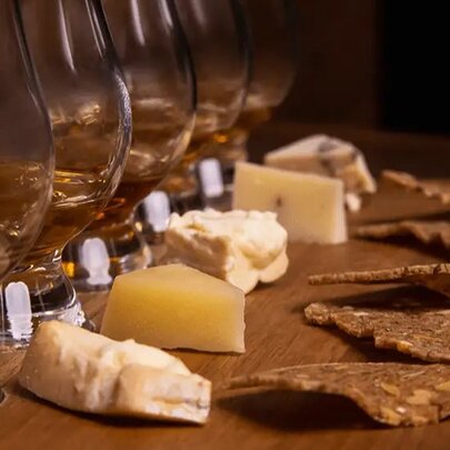 A flight of five whiskies with five different cheeses in front of each glass.