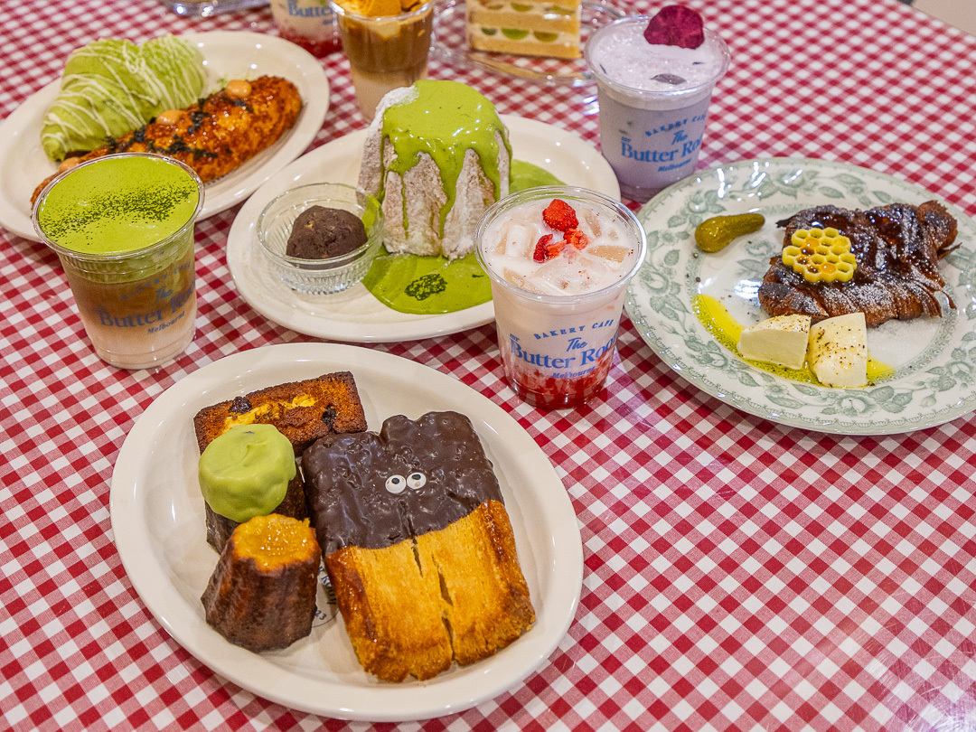 A spread of cakes and drinks on a red tablecloth.
