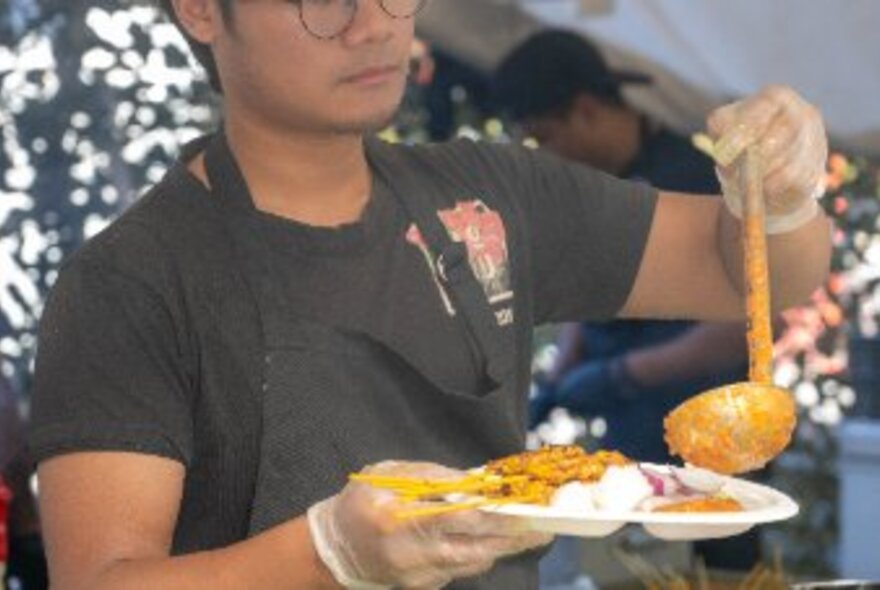 A person in a black apron dishing up food onto a plastic plate at the Indonesian Street Food Festival at Queen Victoria Market.