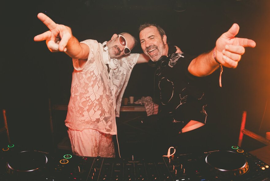 Two DJs hugging and with arms outstretched towards the camera.