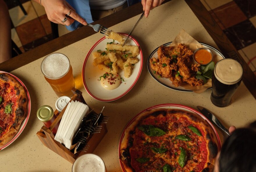 Overhead view of a table with plates of food and glasses of beer, inside a bar.
