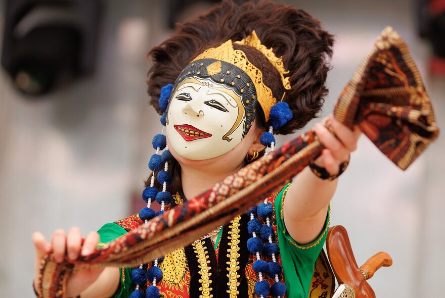 A traditional Indonesian performer wearing a painted mask and holding a silk scarf.