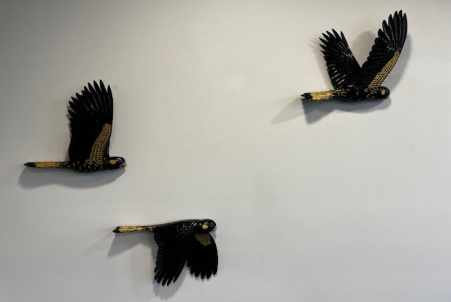 Three wooden bird sculptures flapping across a gallery wall.