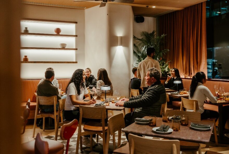 Interior of a warmly lit restaurant filled with people eating and drinking at tables.