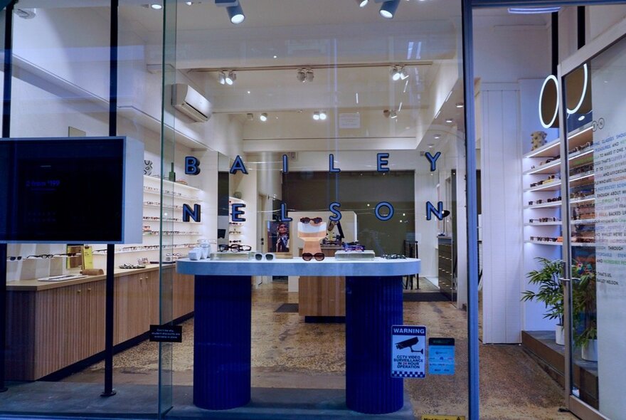The shopfront of an eyeglass store, with large windows and shelves of eyeglasses, as seen from the street outside.