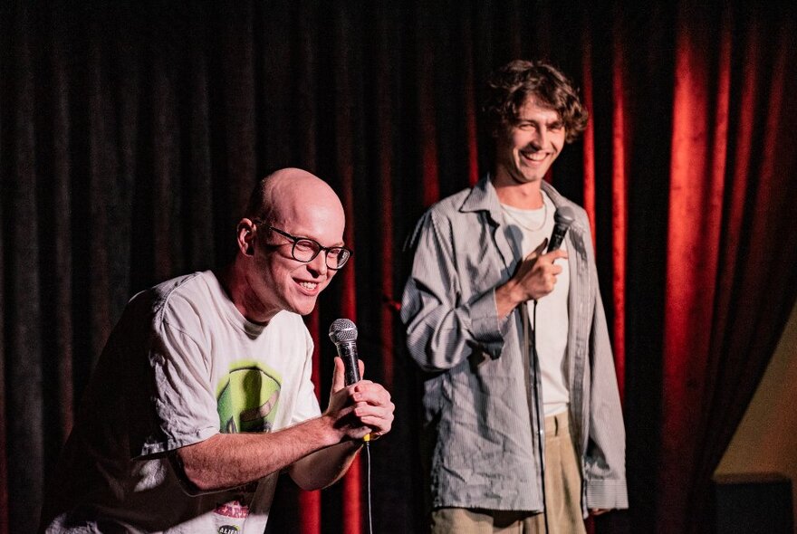 Comedian Danny Sewell, a young man performing stand-up comedy on stage, with another person standing next to him.