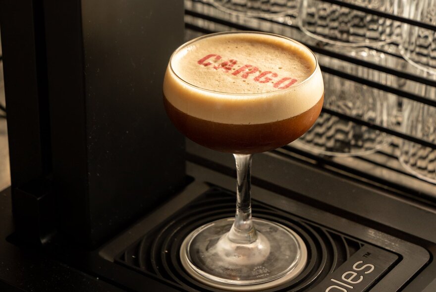 An espresso martini in a glass with the words cargo dusted onto the frothy top.