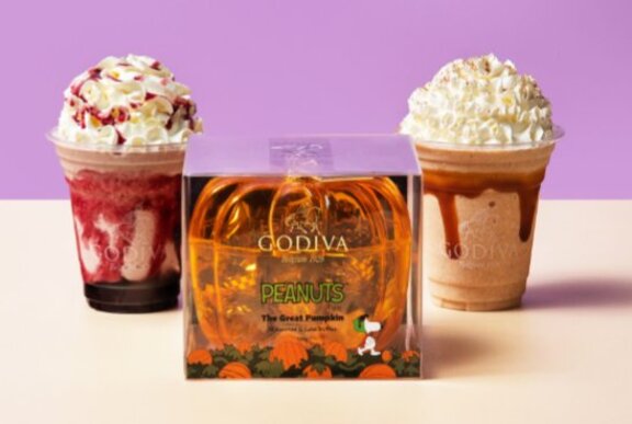 Two cream-topped drinks next to a plastic orange gift box.