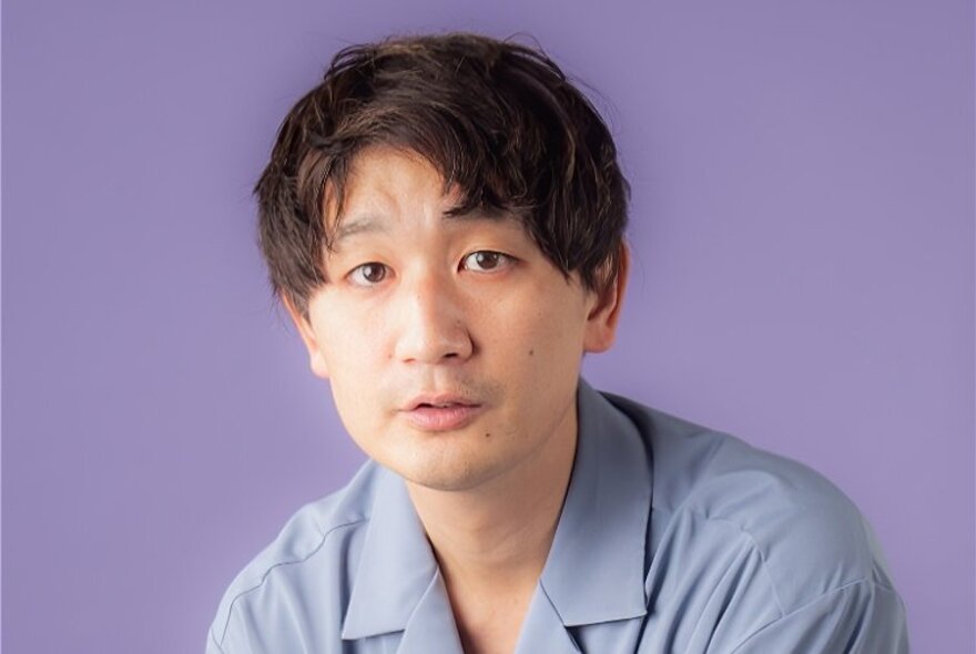 Comedian Takashi looking a bit dazed in front of a purple background. 