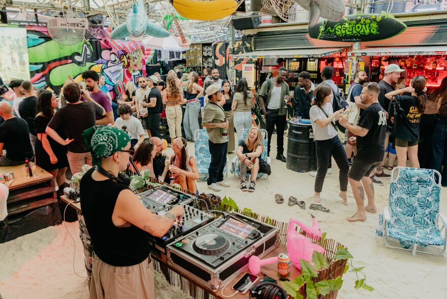 Revellers at an open-air Melbourne bar that has been transformed into a beach party with sand on the floor.