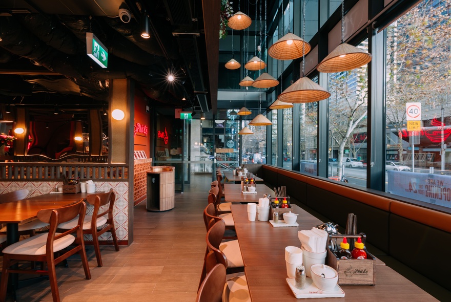 An empty restaurant with stools on narrow counters and many small lamp shades hanging from the ceiling. 