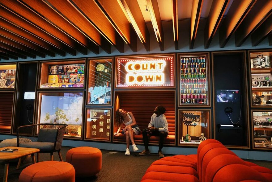 Two people seated below a neon sign.