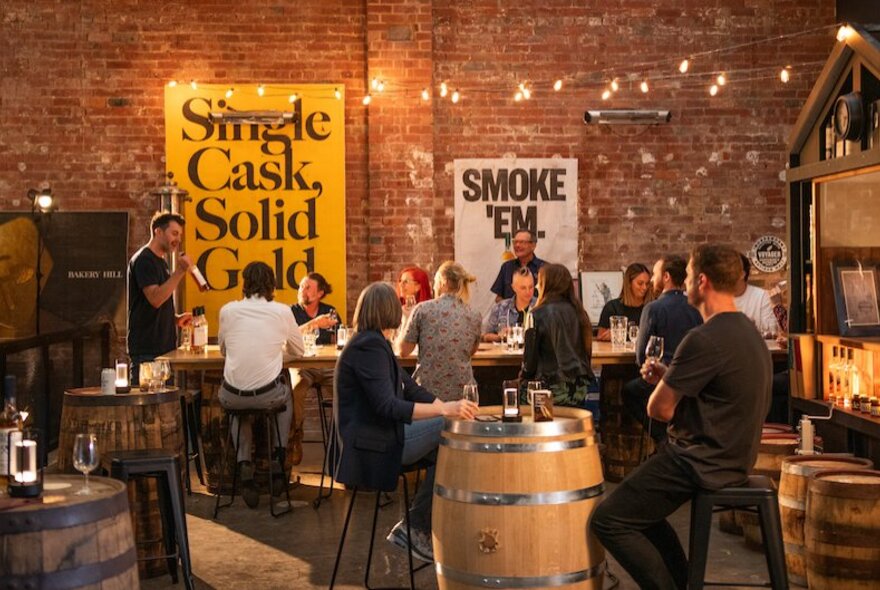 People seated in a distillery with brick walls, casks and tasting tables.