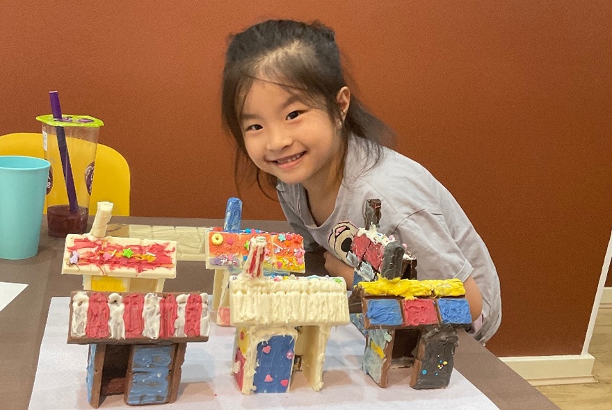 A girl smiling proudly next to small painted houses.