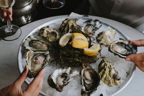A dozen natural oysters on a plate of salt with a salad of seaweed and lemon in the middle.