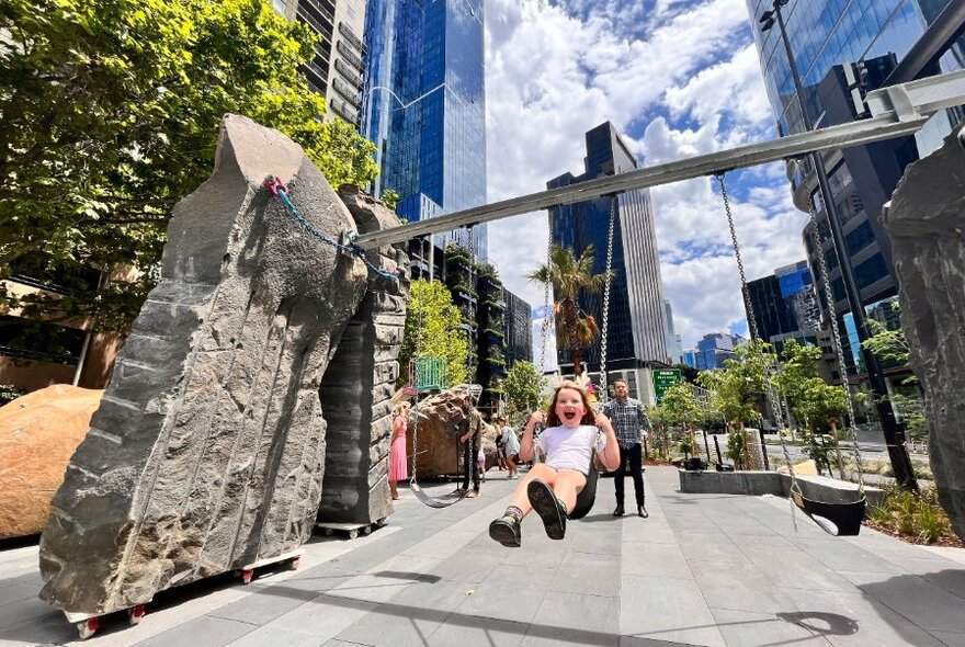 Child smiling while being pushed in a swing in a playground space in an urban city setting.