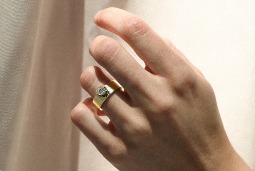 A hand with a gold diamond ring on one finger.