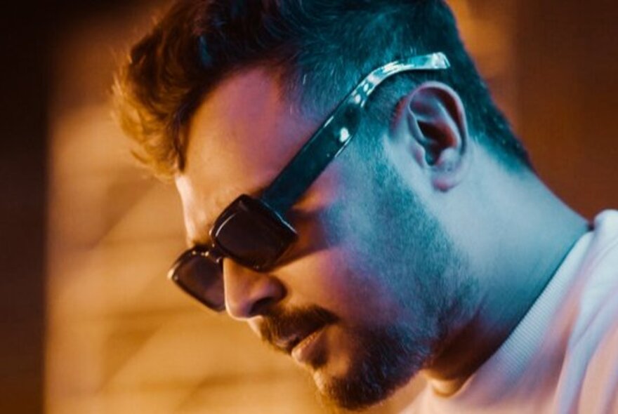A serious man wearing sunglasses looking downwards. 