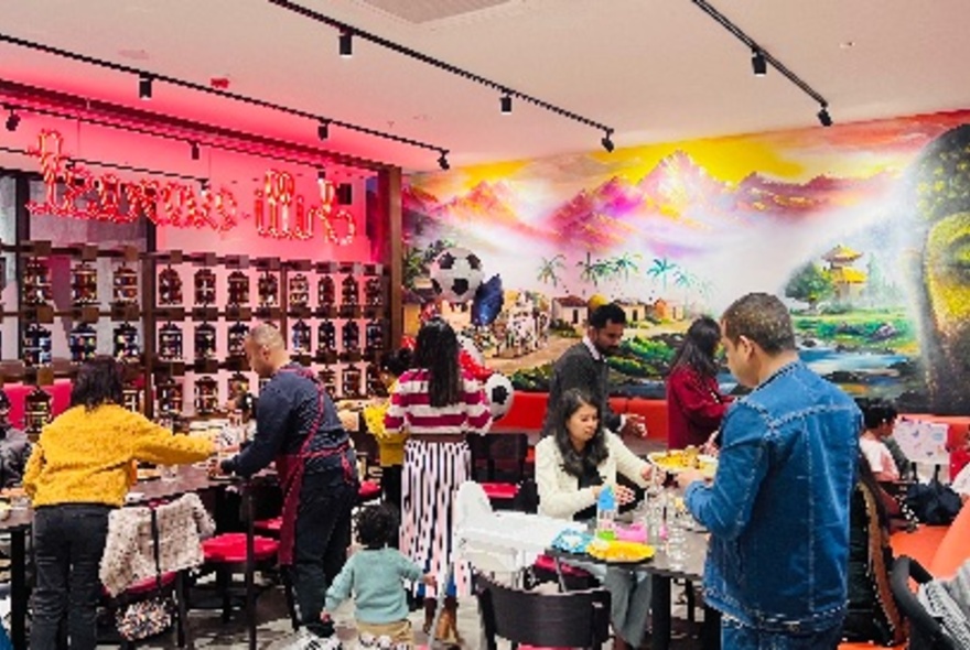 Brightly decorated restaurant interior, with a large mural on the rear wall, and patrons eating at tables.