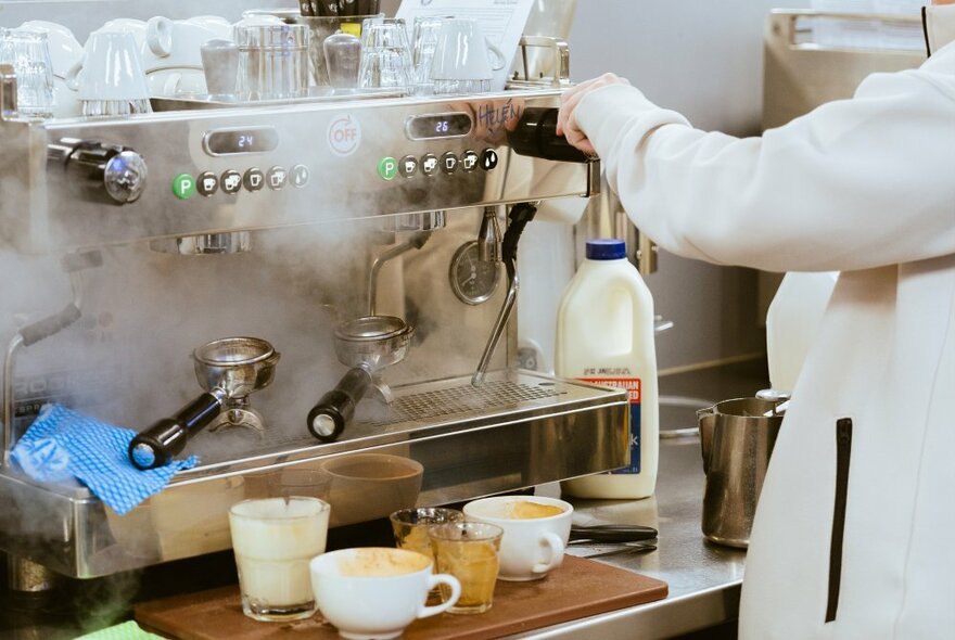 A commercial espresso machine with a person in a white coat making coffees.