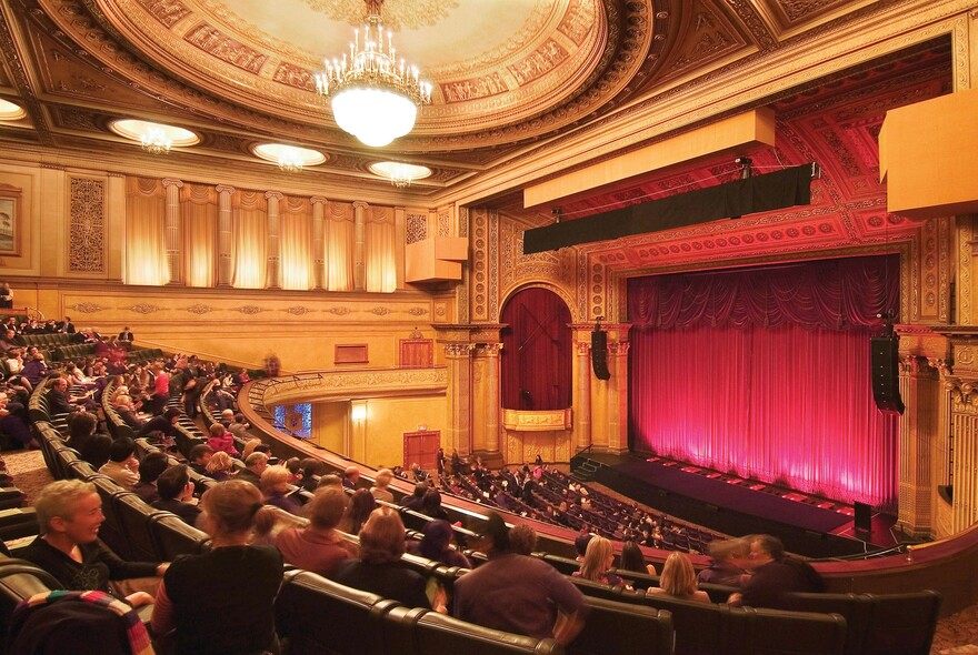 Audience in curved rows of seating looking towards the stage curtain inside the Regent Theatre.