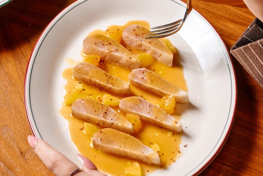 A white bowl of kingfish ceviche in an orange sauce.