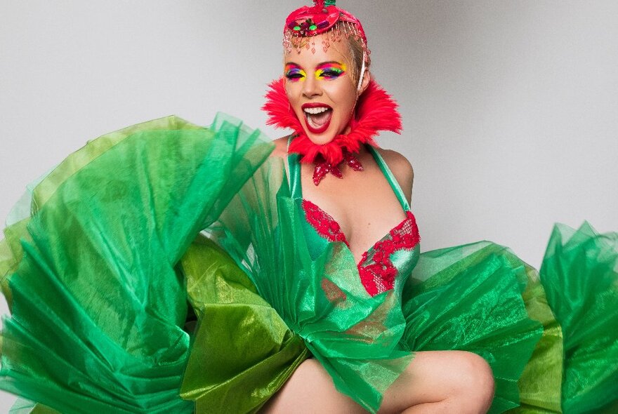 Burlesque performer wearing red and green outfit with cape and Elizabethan collar and sequinned headdress.