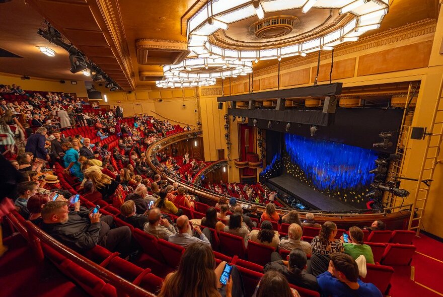 Crowds filling the seats in a grand theatre. 