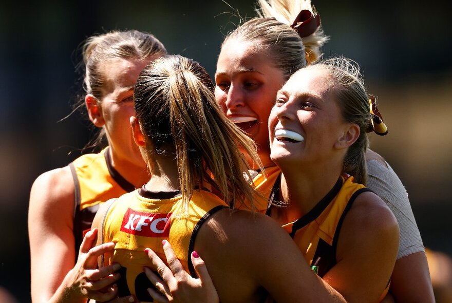 A huddle of AFLW Hawthorn players celebrating during a match.