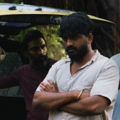 A still from the acclaimed Tamil movie, Members of the Problematic Family, showing a man with his arms crossed, and three others behind him standing at the boot of a car.