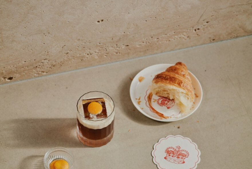 Concrete table with a glass and half-eaten croissant.