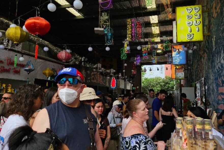 People walking around at a festival at EziStreat with food stalls and hanging lanterns in the background.