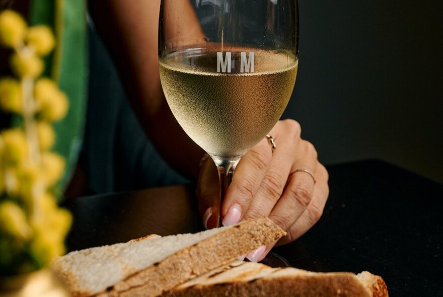 A woman's hand holding a glass of cold white wine with a panini sandwich in front of her.
