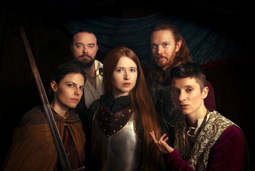 Actors dressed in medieval costumes posing grouped together with serious expressions. 