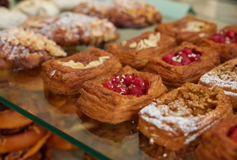 Close up shot of pastries with raspberries, almonds, and powdered sugar on them, placed on a glass shelf.