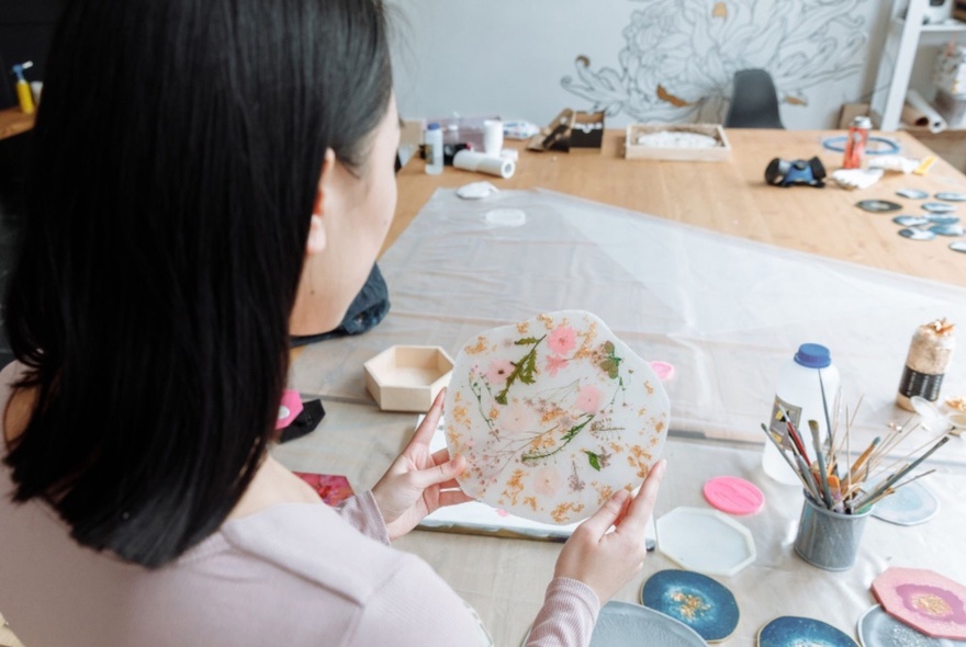 A person holding a plate decorated with a floral design over a crafts table.