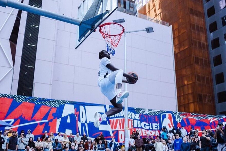 A man leaping into the air to take a slam dunk at a basketball hoop in front of an audience.