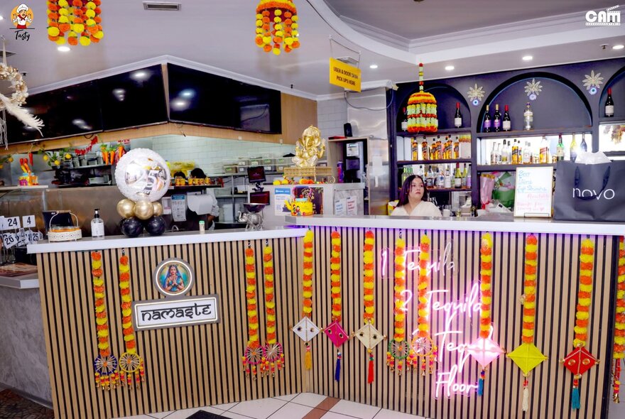 The restaurant counter at an Indian resturarant hung with yellow and red flower garlands.
