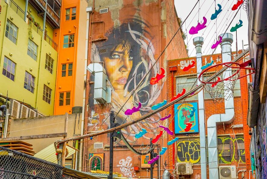 A mural of a woman's face on the side of a building with small abstract art suspended in the air.